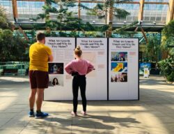 Two people stand in front of an exhibition panel. The panels display both text and image. The images are 'generic images' from news outlets and the accompanying text explains them.